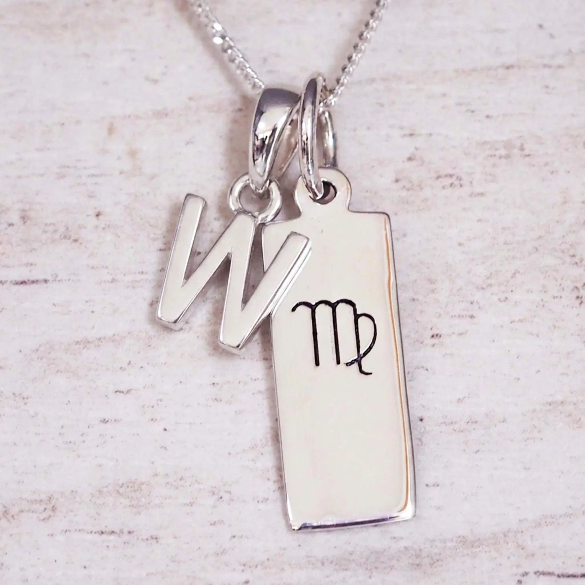 sterling silver initial w virgo zodiac star sign pendant necklace against a light wooden background