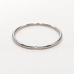 A minimalist polished silver band ring with a single small clear gemstone set in the center, displayed on a clean white background.