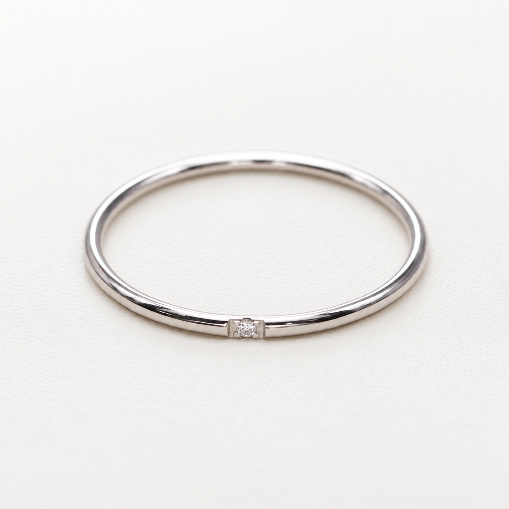 A minimalist polished silver band ring with a single small clear gemstone set in the center, displayed on a clean white background.