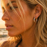 Close-up of a woman's face at the beach with a sunset, wearing a stainless steel silver waterproof hoop earring