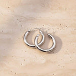 Silver hoop earrings on a beige stone surface
