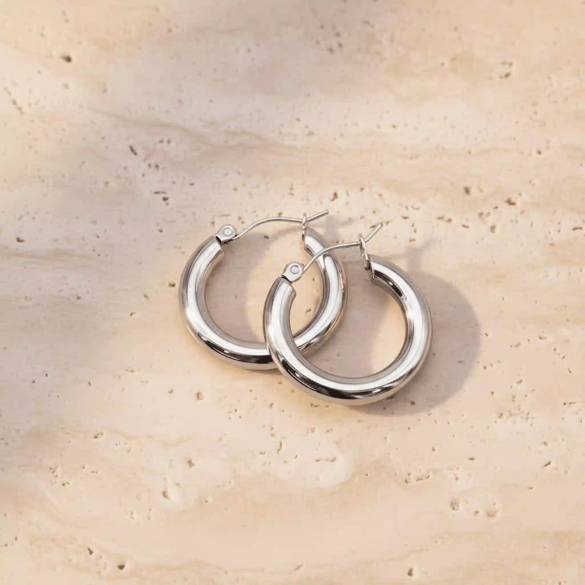 Silver waterproof hoop earrings on a beige stone surface