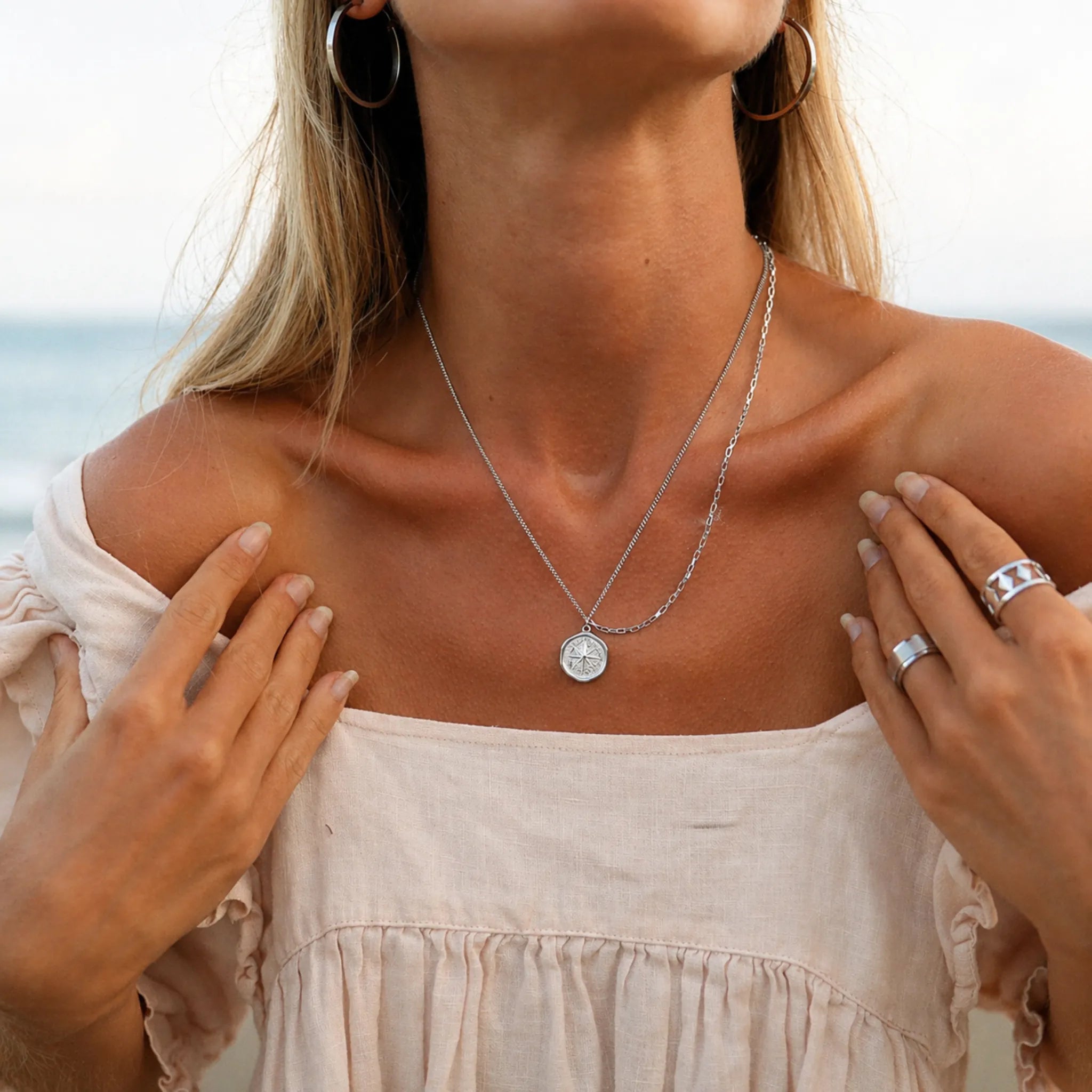 woman on the beach wearing a stainless steel silver waterproof necklace with a starburst compass pendant