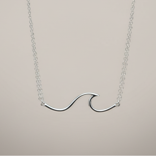 sterling Silver wave-shaped necklace on a wooden surface with dried flowers in the background by indie and harper australia