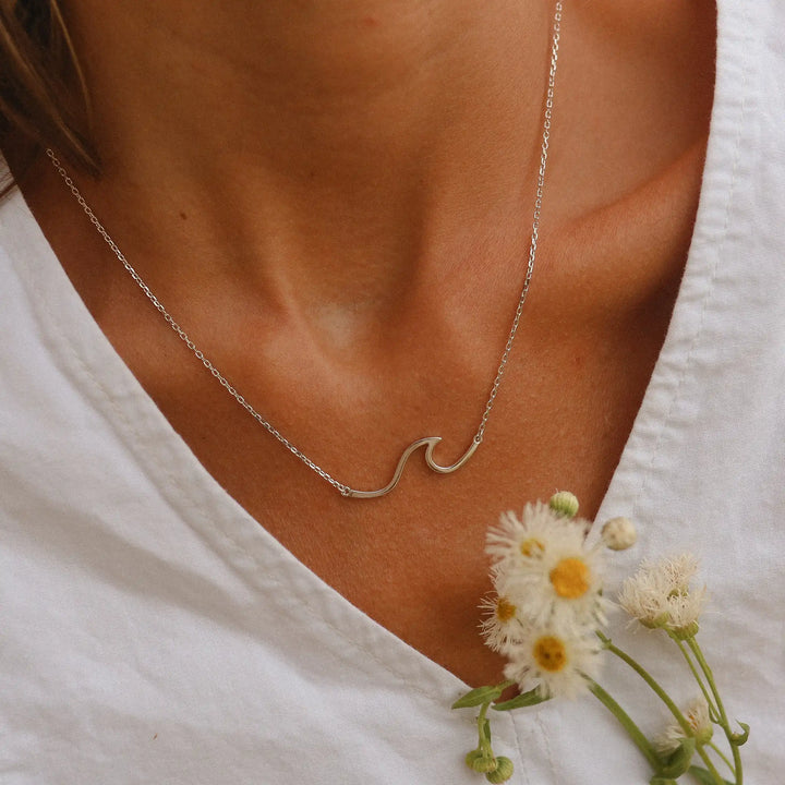 Woman in a white top holding flowers wearing a sterling silver necklace in the shape of a wave - Australian jewellery brand