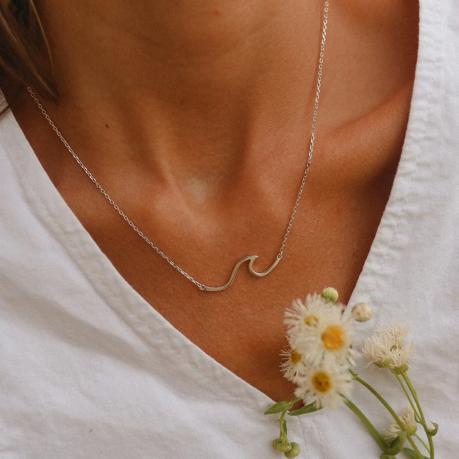 Woman in a white top holding flowers wearing a sterling silver necklace in the shape of a wave - Australian jewellery brand