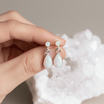 Opal earrings held between fingers with a neutral background