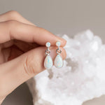 Opal earrings held between fingers with a neutral background