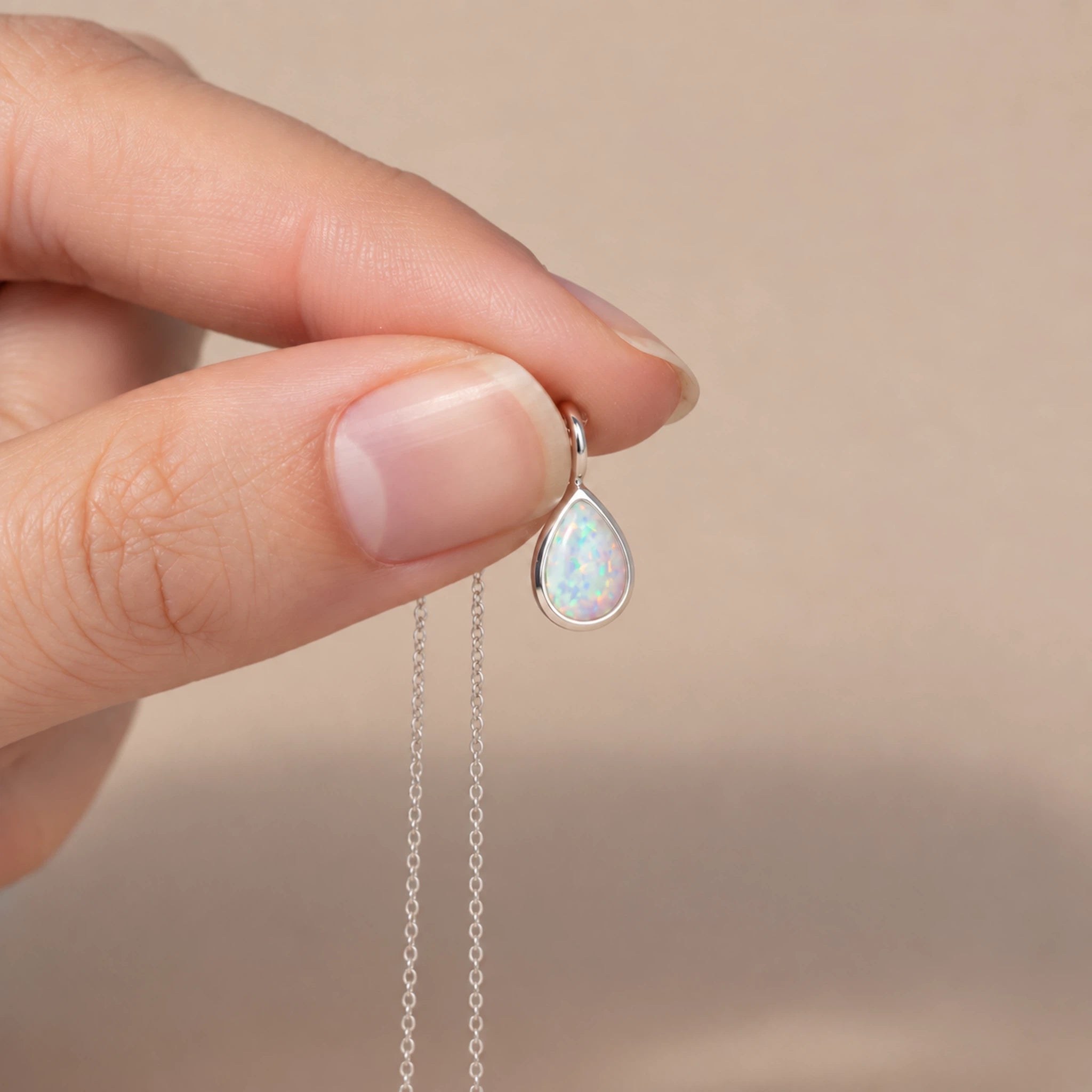 sterling silver white opal necklace held by fingers holding a dainty bezel-set teardop shaped cabochon white opal pendant necklace