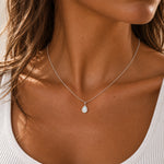 silver opal necklace worn by a woman featuring a delicate silver chain necklace with a small teardrop-shaped white opal pendant.