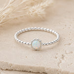 Sterling Silver beaded band ring with a central round white opal stone on a beige textured background