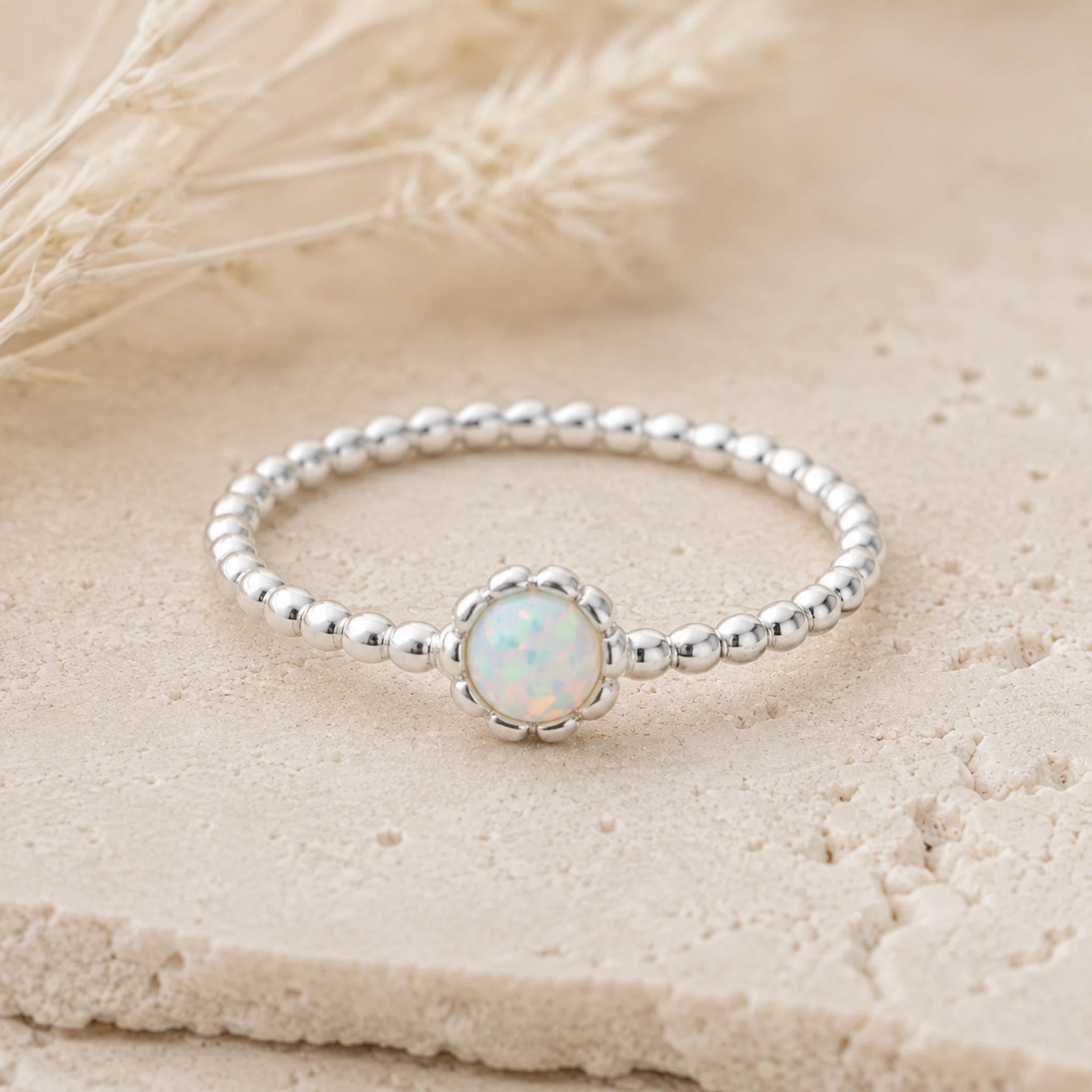 Sterling Silver beaded band ring with a central round white opal stone on a beige textured background