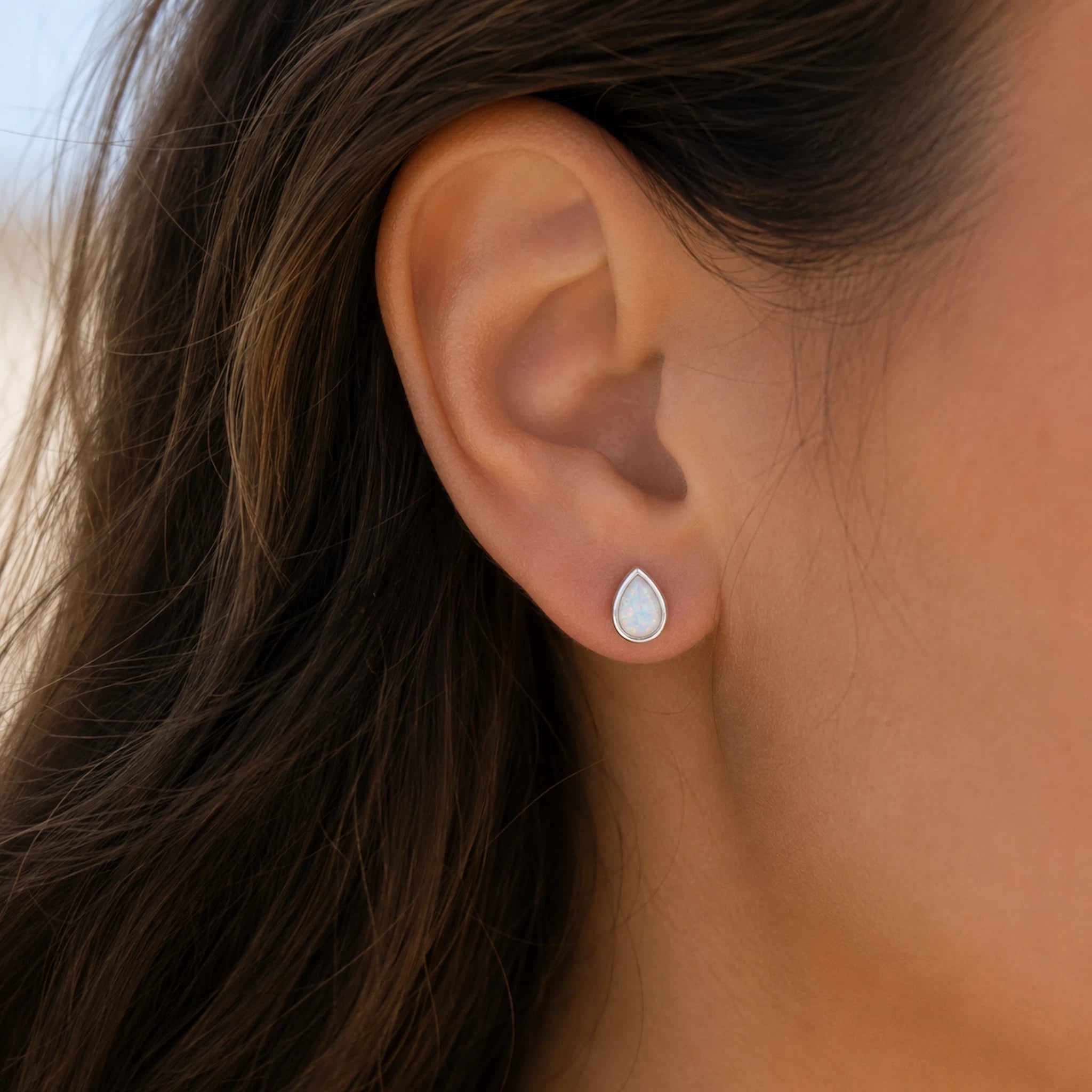 sterling silver teardrop stud earring with a bezel set white opal being worn