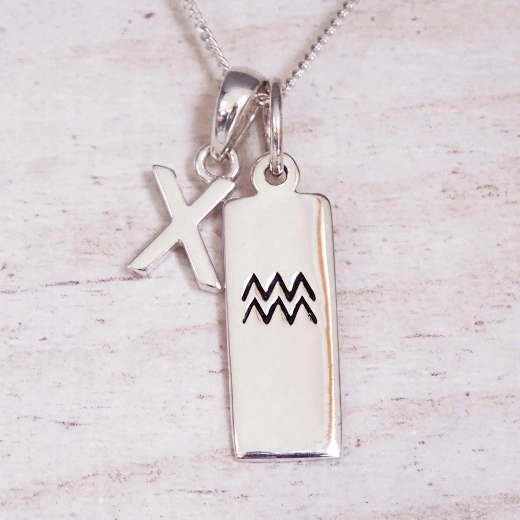 Sterling Silver X Initial and Aquarius Necklace on a fine silver chain against a light wooden background