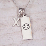 Sterling Silver X Initial Cancer Zodiac Star Sign Necklace on a fine silver chain against a light wooden background
