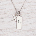 sterling silver initial X pendant and capricorn necklace on a fine silver chain against a light wooden background