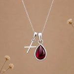 sterling silver initial x january birthstone natural garnet pendant necklace against a dark warm beige background