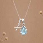 sterling silver initial x march birthstone natural aquamarine pendant necklace against a dark warm beige background