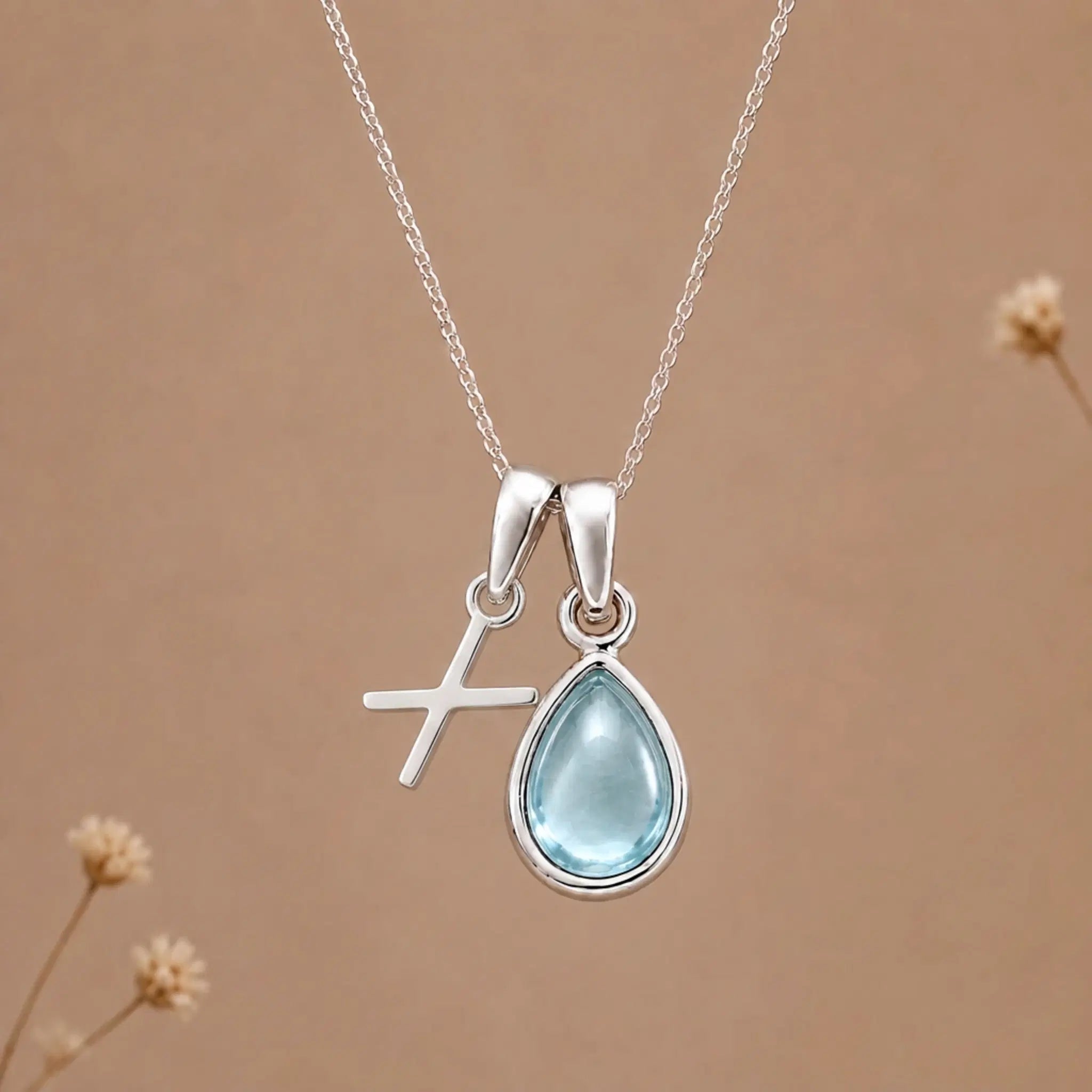 sterling silver initial x march birthstone natural aquamarine pendant necklace against a dark warm beige background