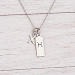 sterling silver X initial Pisces Necklace on a fine silver chain against a light wooden background