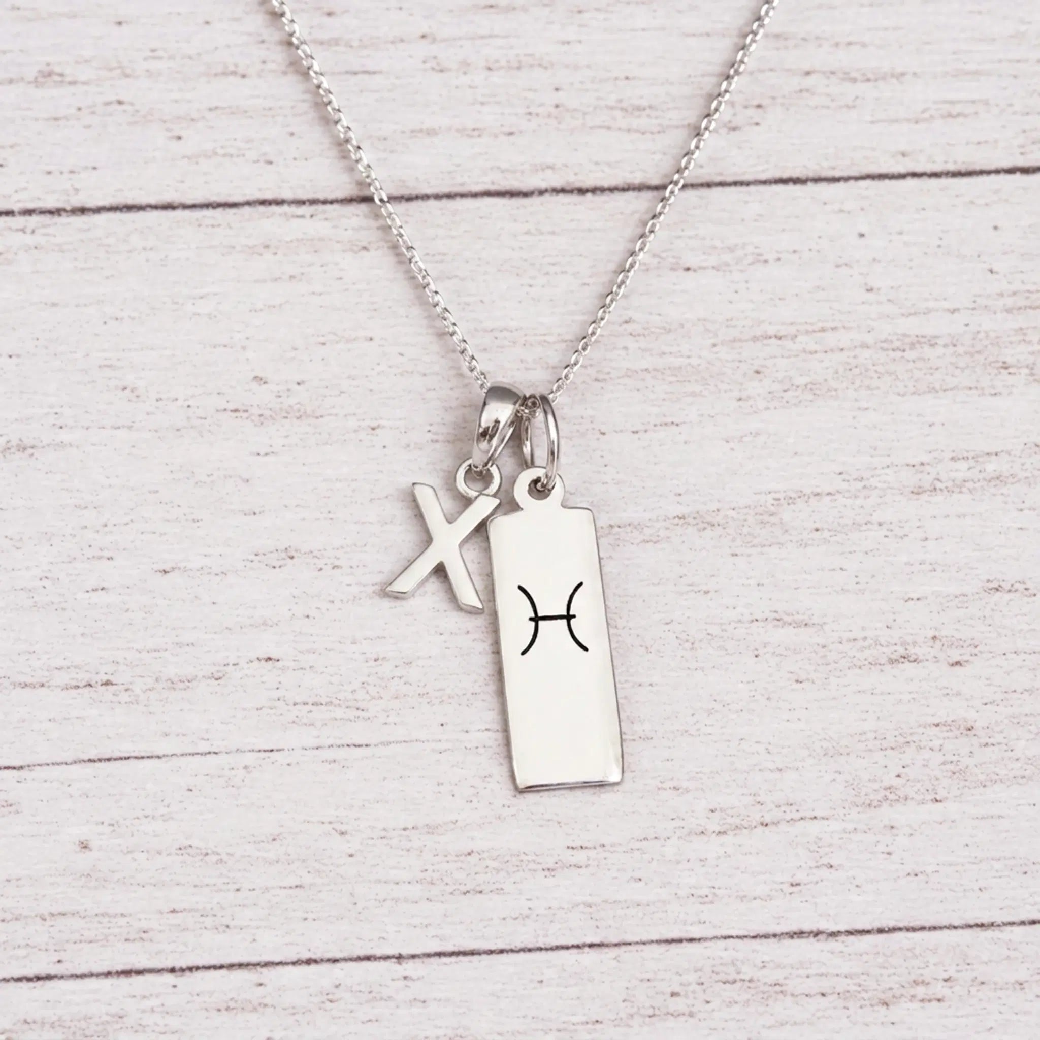 sterling silver X initial Pisces Necklace on a fine silver chain against a light wooden background