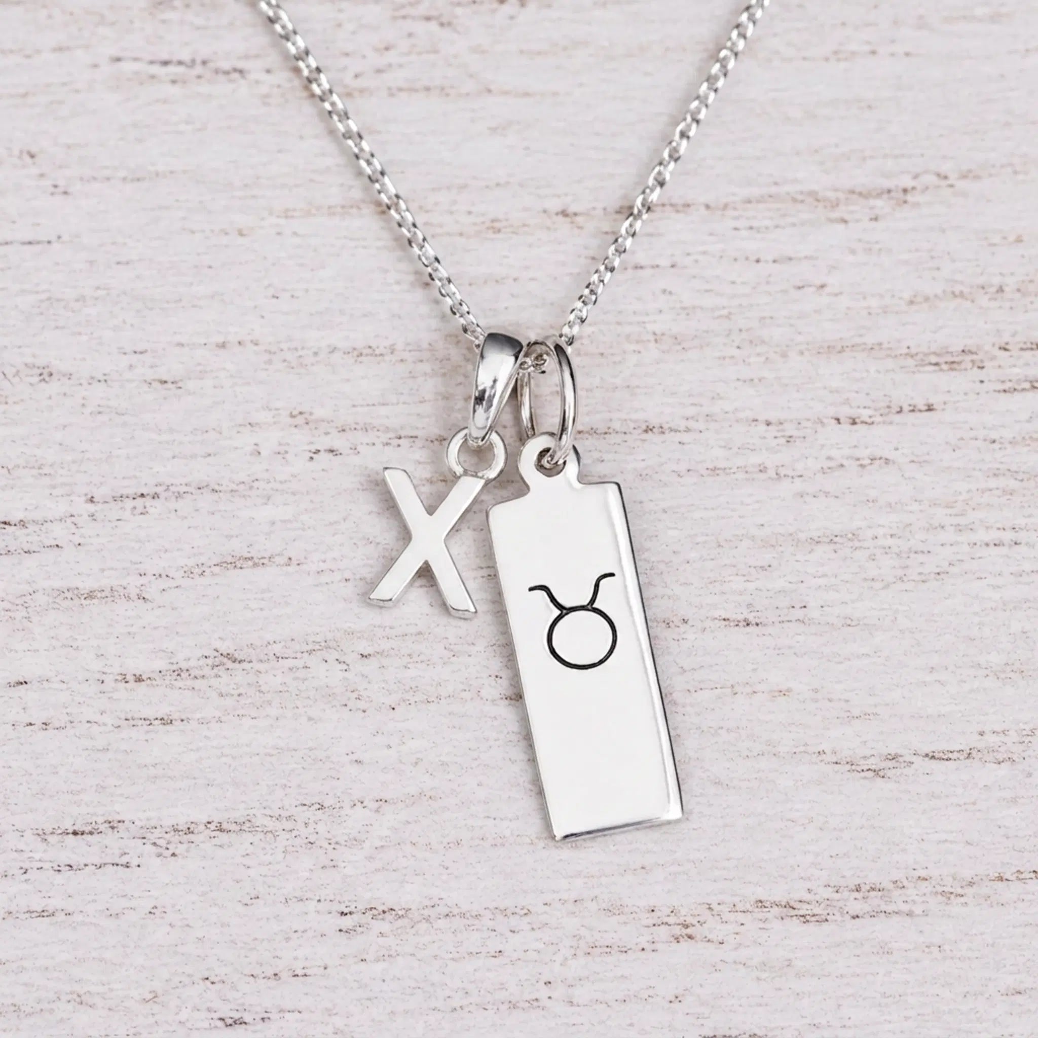 Sterling silver X initial Pendant and Taurus Necklace on a fine silver chain on a light wooden background