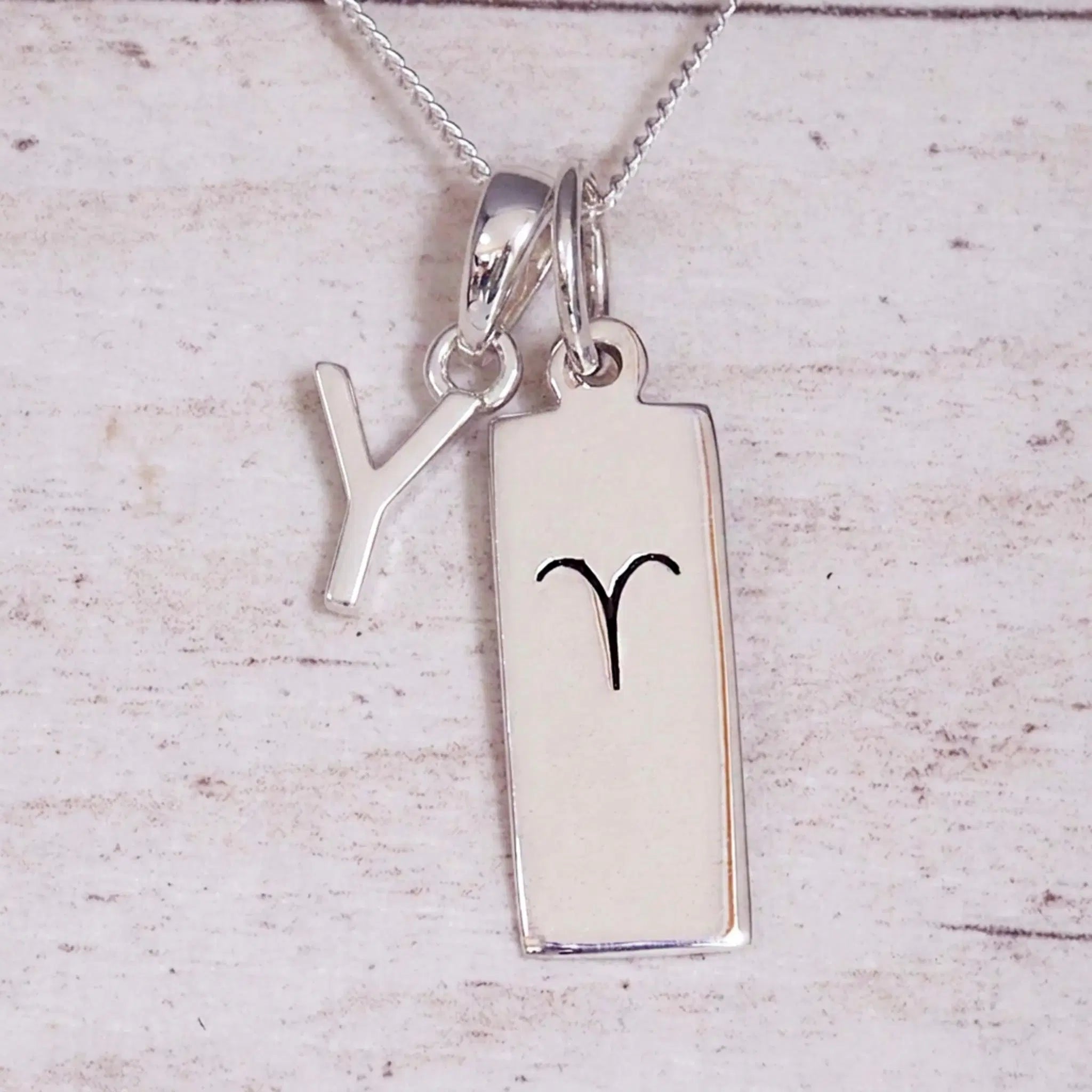 Sterling Silver Y Initial pendant and Aries necklace on a fine silver chain on a light wooden background