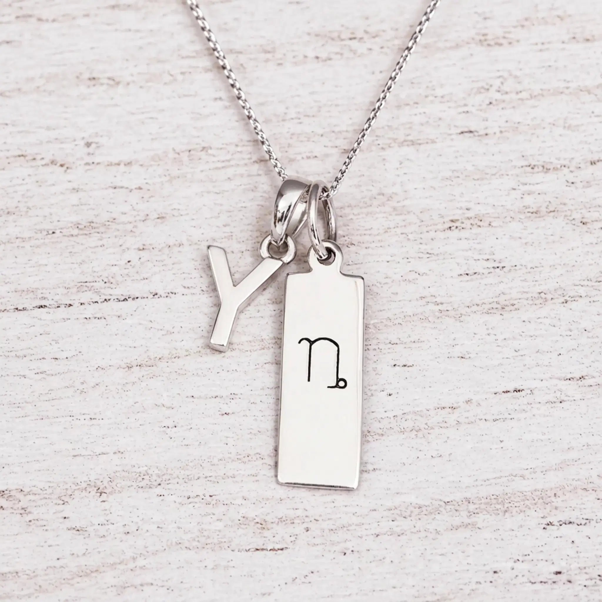 sterling silver initial Y pendant and capricorn necklace on a fine silver chain against a light wooden background