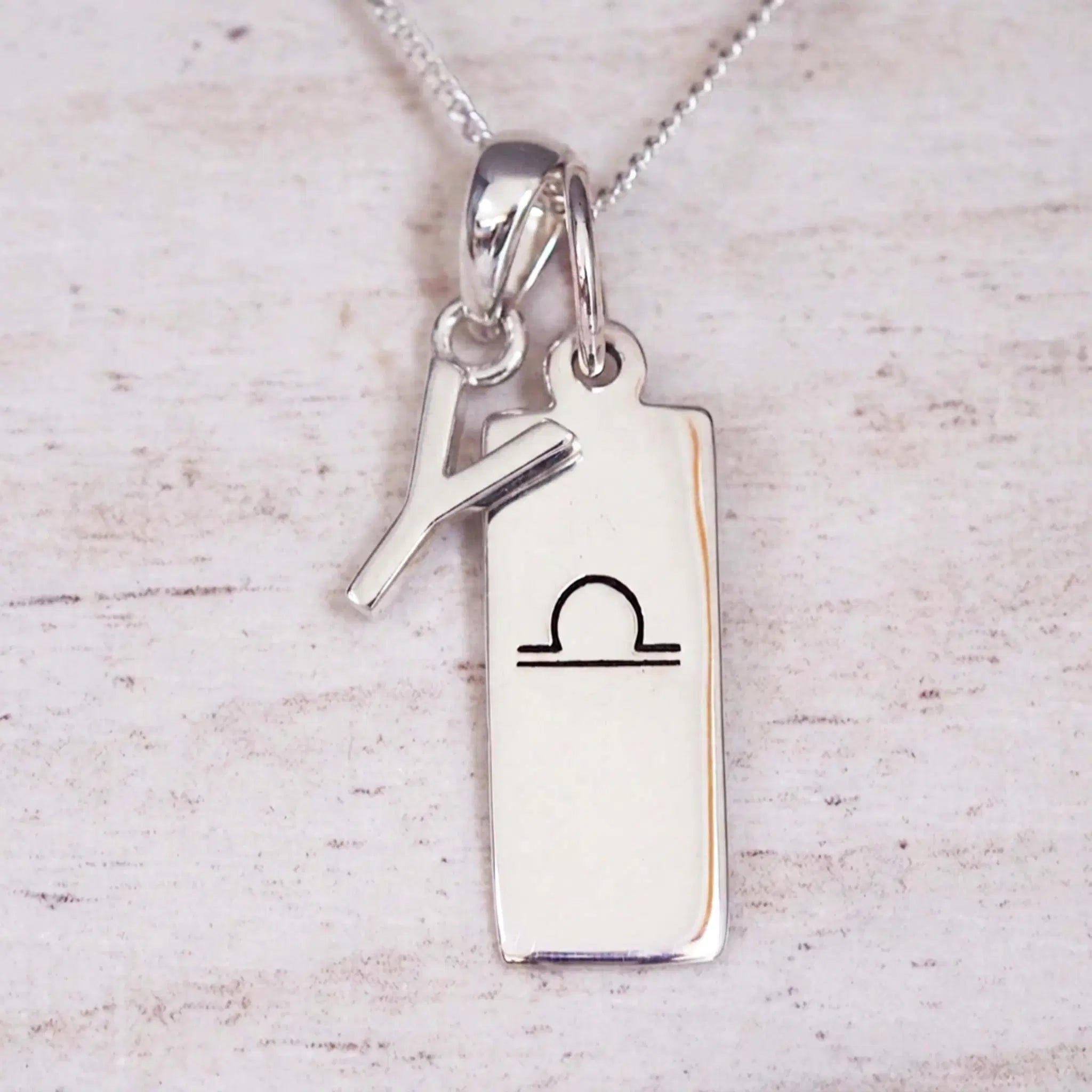 sterling silver initial y libra zodiac star sign pendant necklace against a light wooden background