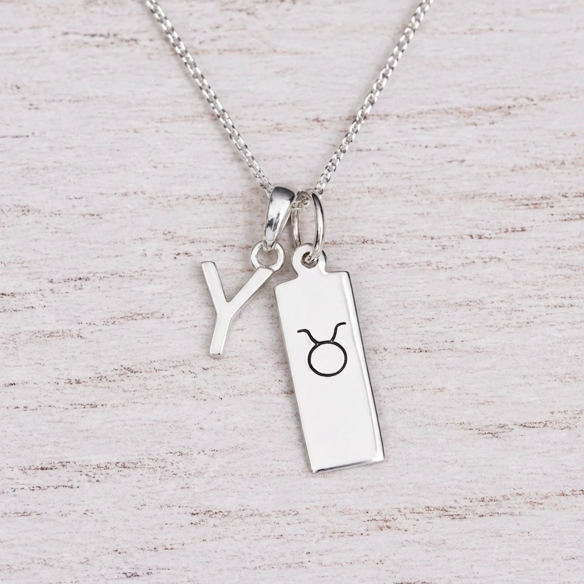 Sterling silver Y initial Pendant and Taurus Necklace on a fine silver chain on a light wooden background