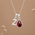 sterling silver fine chain double pendant necklace, with a uppercase Z letter pendant and a pear shaped january birthstone natural garnet gemstone on a light background.