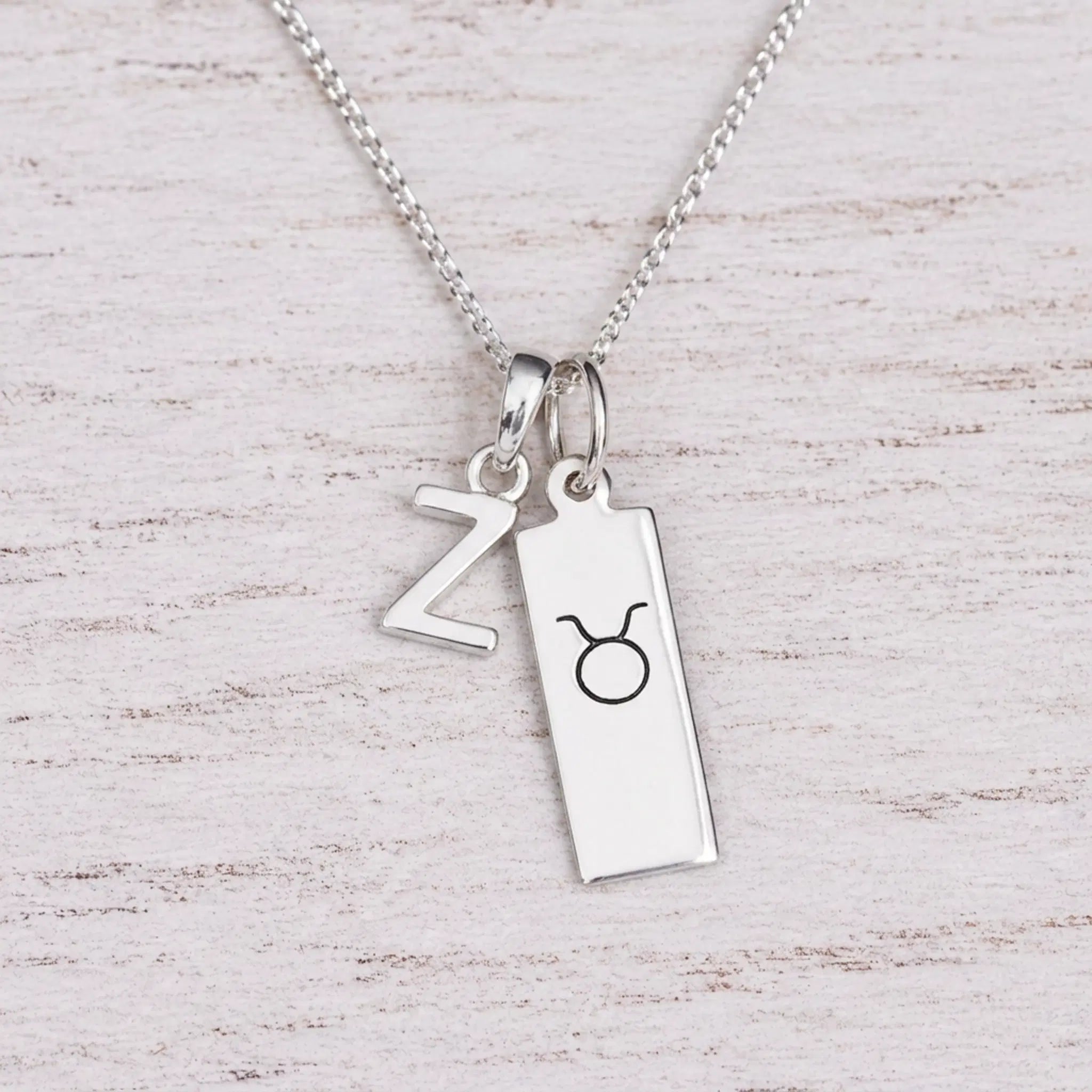 Sterling silver Z initial Pendant and Taurus Necklace on a fine silver chain on a light wooden background