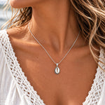 Small 10 × 14 mm cowrie shell necklace in sterling silver on a fine curb chain, worn with a white lace top