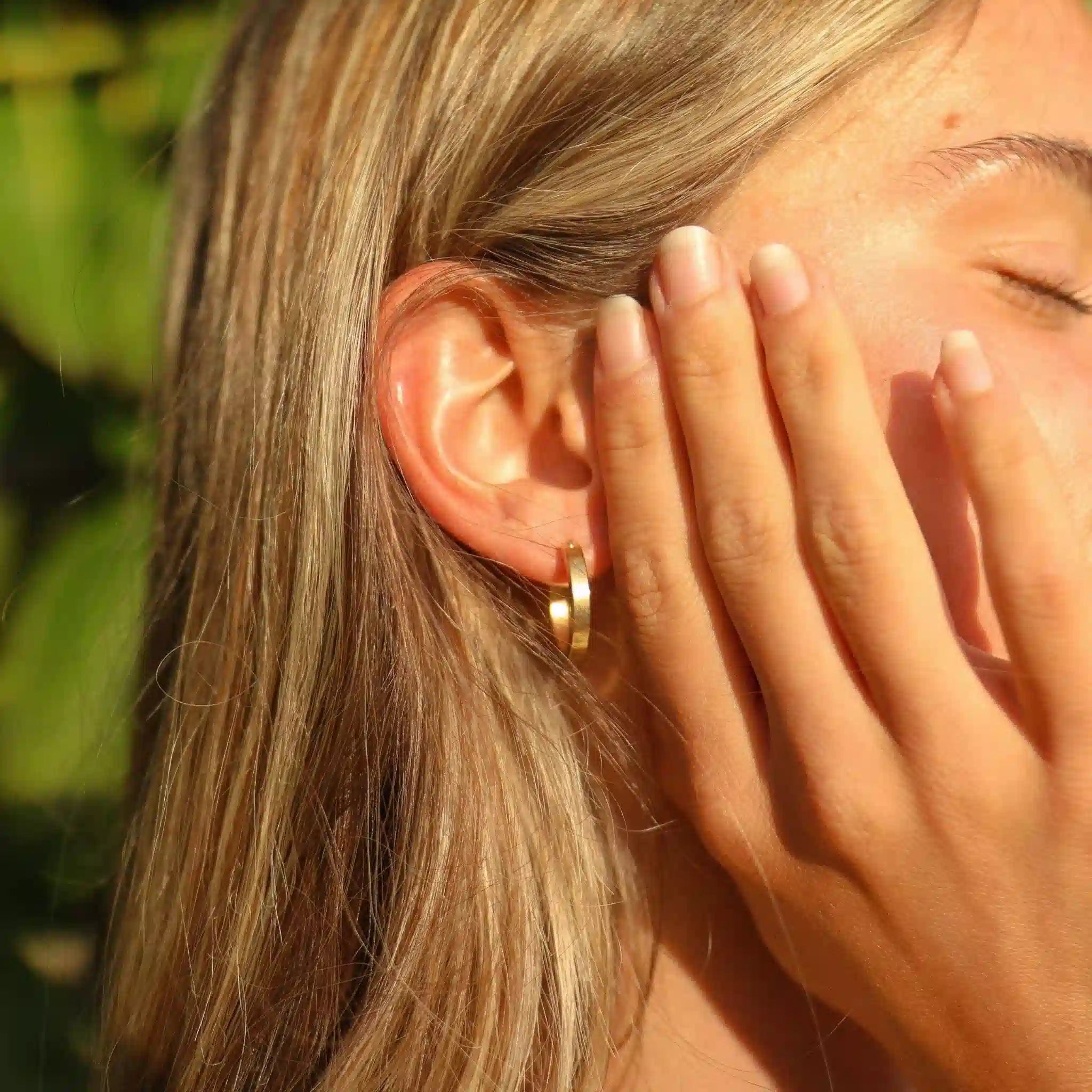 Close-up of a person wearing a small gold hoop earring with a blurred natural background