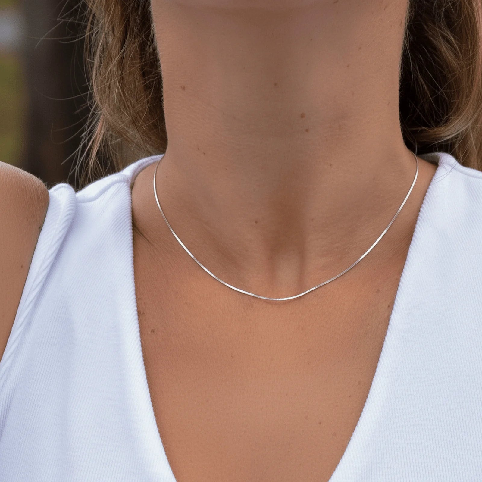Silver necklace worn by a person with a blurred background