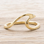 A polished gold wave-shaped ring resting on a light-colored wooden surface.