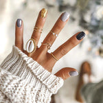Hand with coloured nails wearing the solid 9k gold wave ring and other gold rings