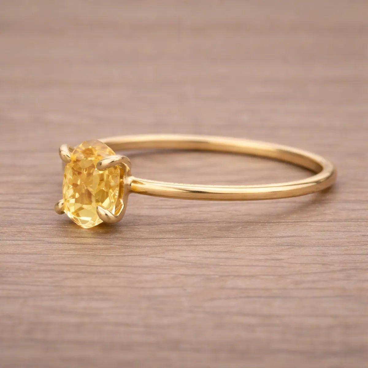 Gold ring with a yellow gemstone on a wooden surface