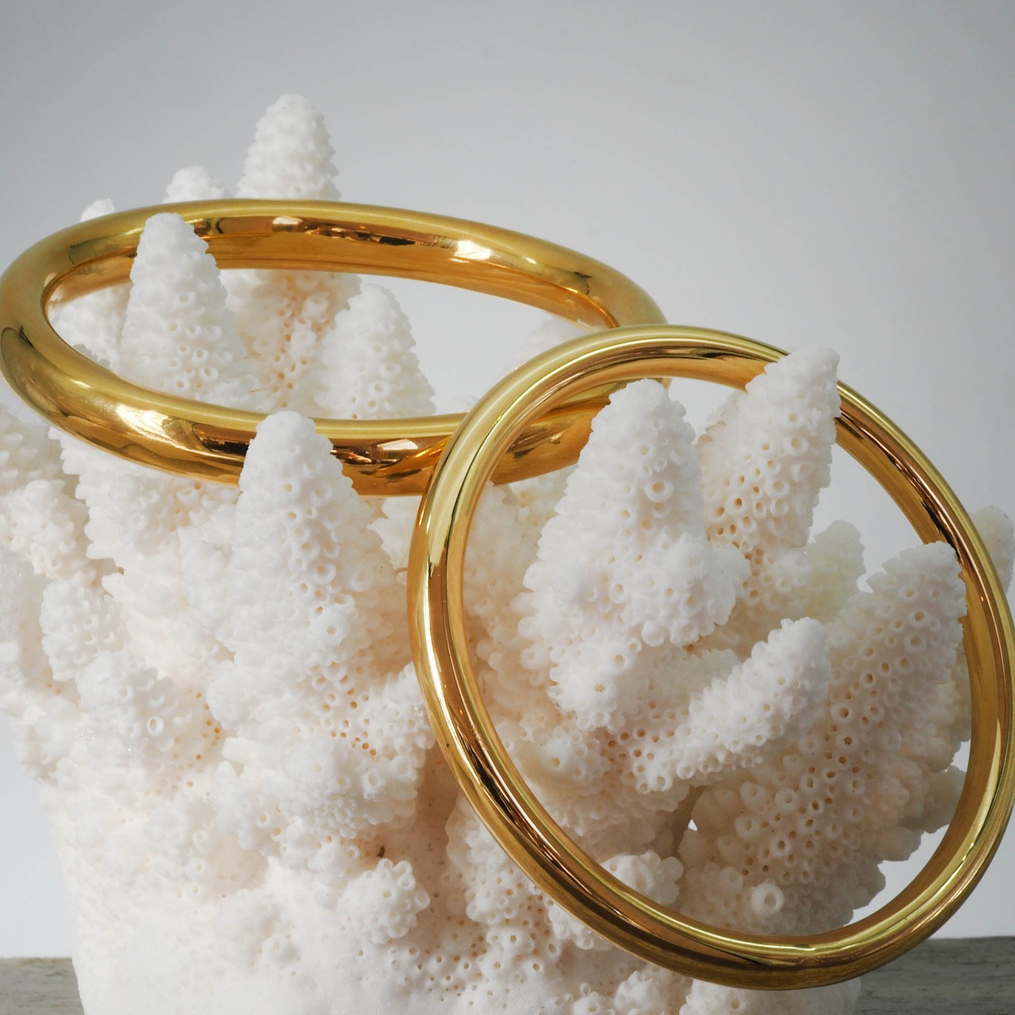 Two waterproof gold bangle bracelets on a white coral-like structure against a light grey background