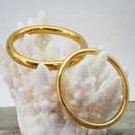 two gold bangle bracelets in polished finish on a coral. gold waterproof jewellery