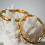 Two gold stainless steel bangles on a white coral-like structure against a light gray background