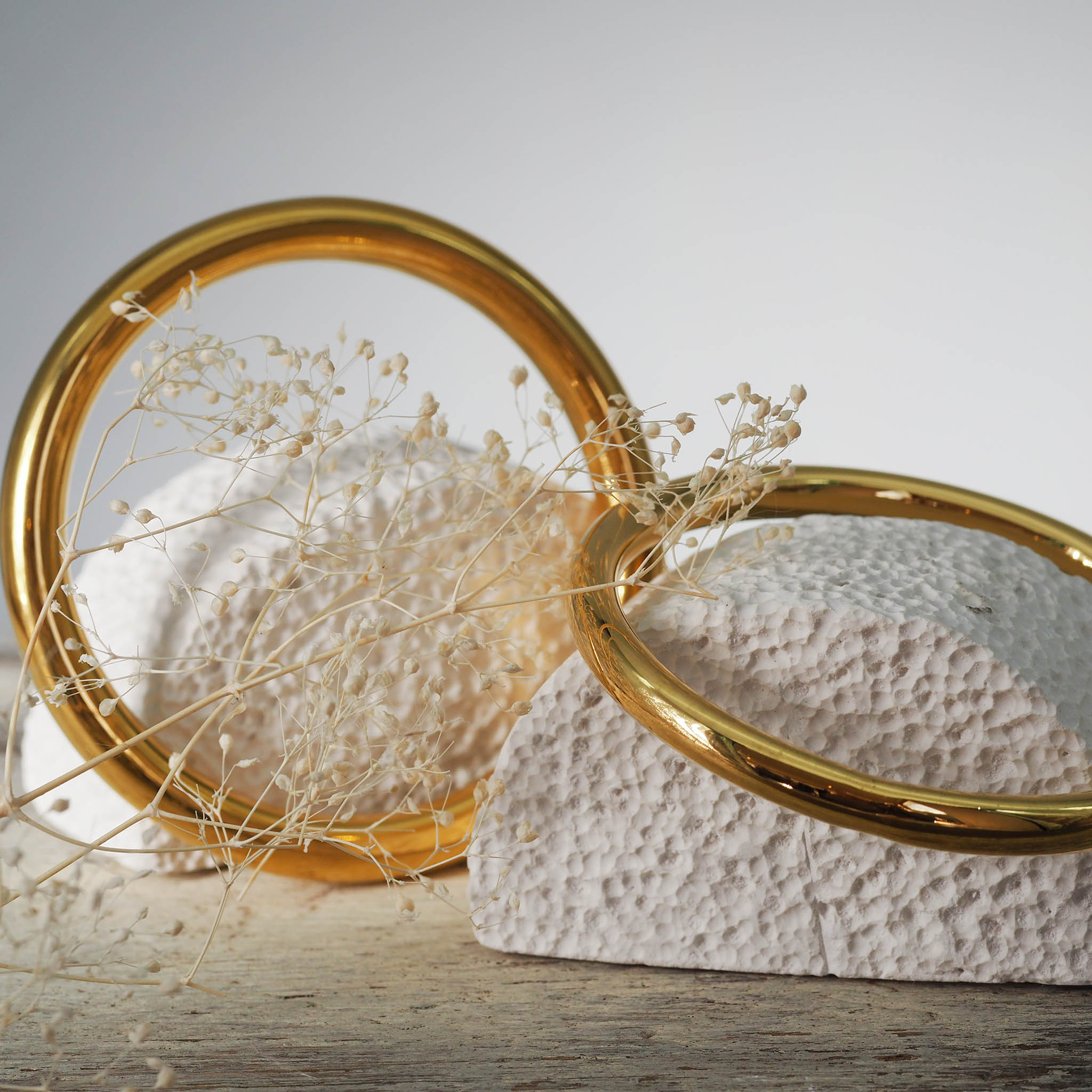 Two gold stainless steel bangle bracelets on a wooden surface.