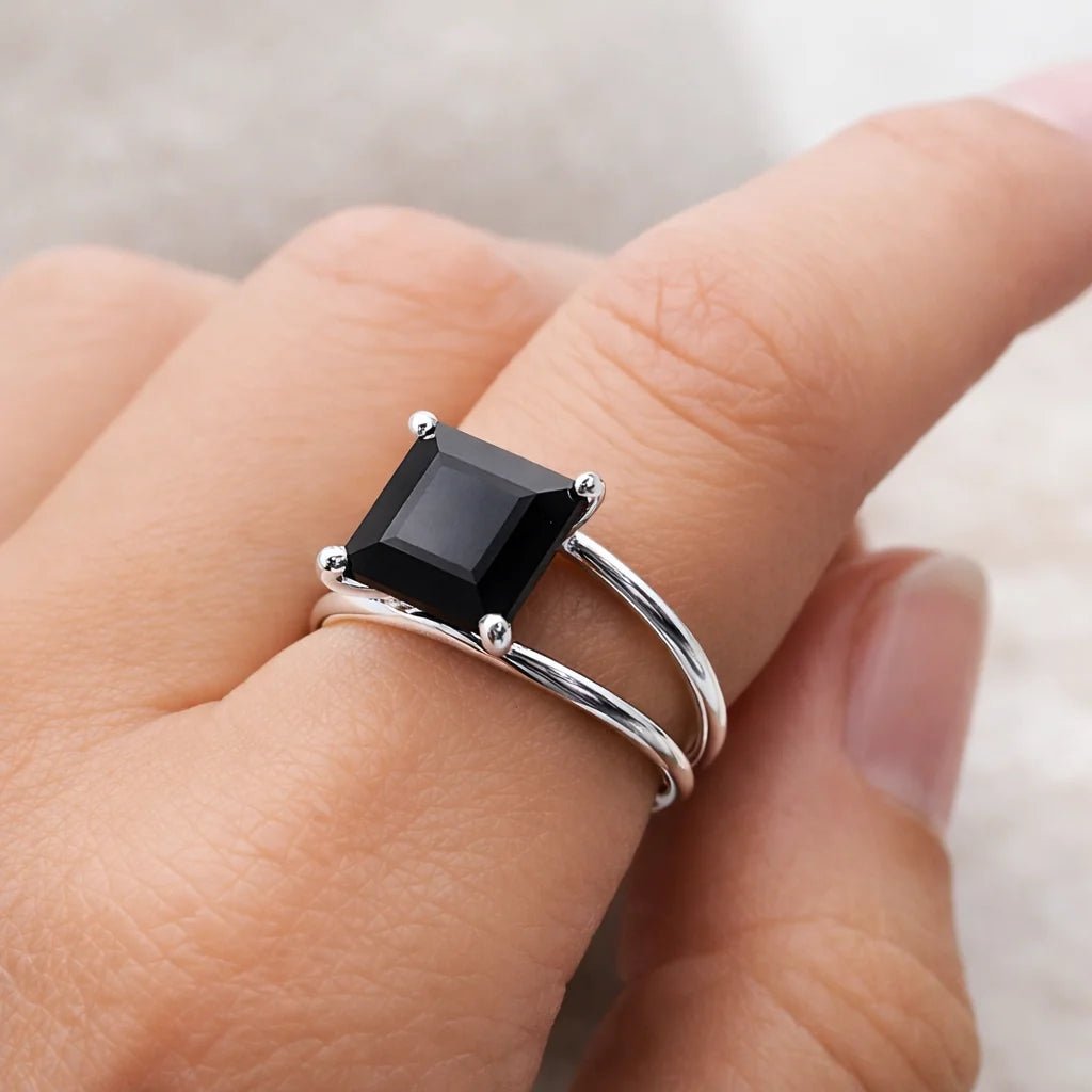 Silver ring with a black onyx gemstone on a finger against a neutral background