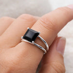 Silver ring with a black onyx gemstone on a finger against a neutral background