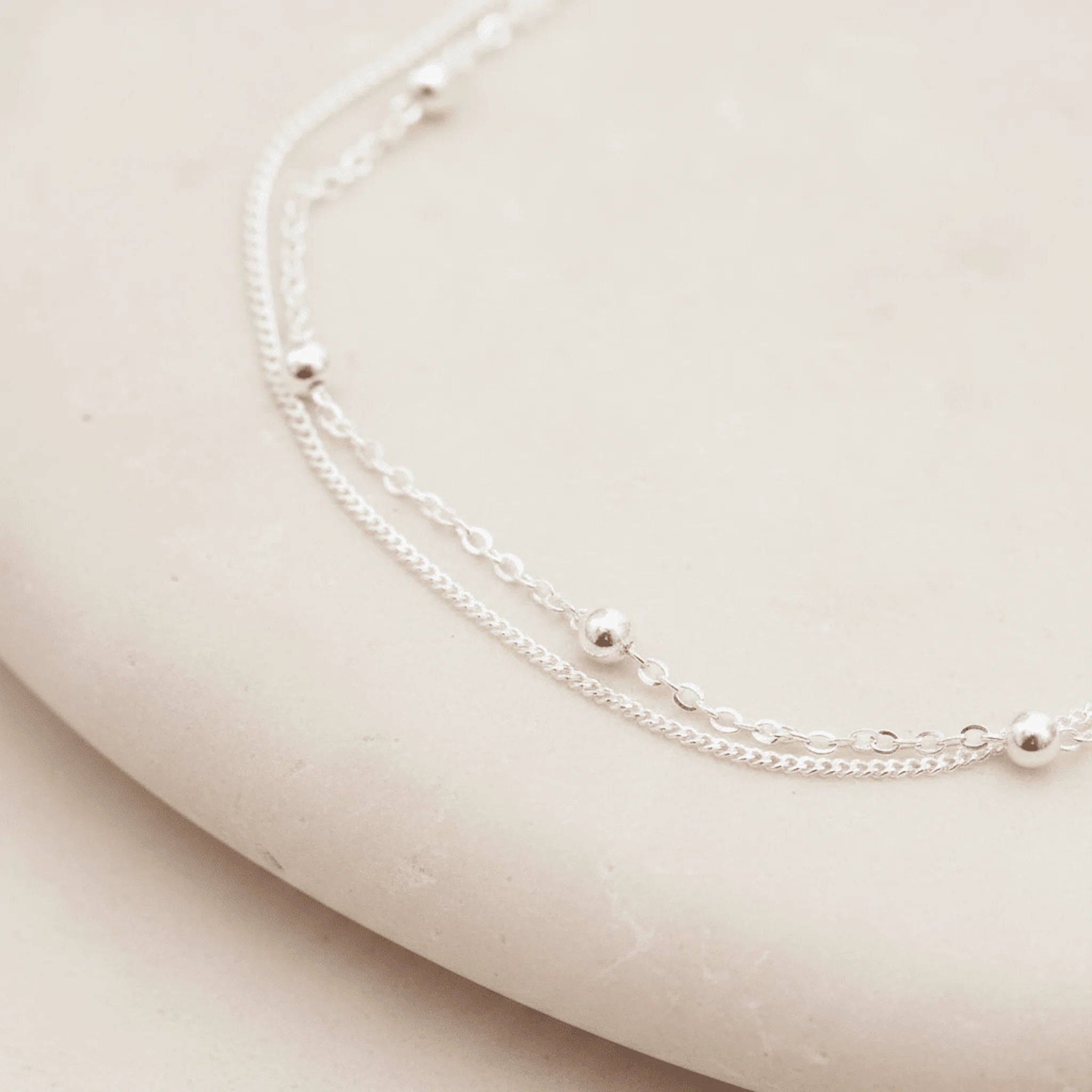 Silver double layer anklet with small beads on a beige surface