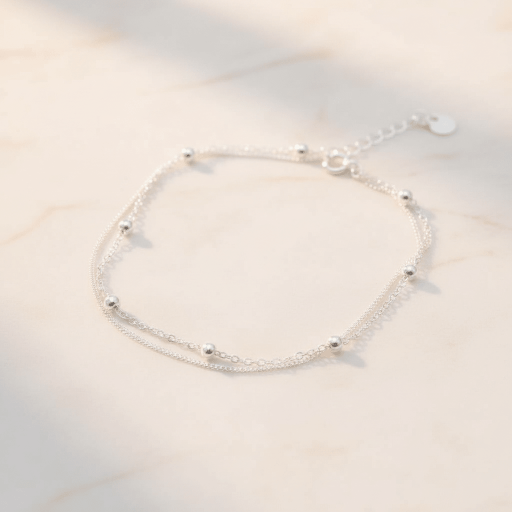 sterling silver anklet with double chain and silver ball beads on a soft white stone surface