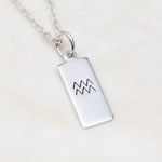 Silver necklace with a rectangular pendant featuring an Aquarius symbol on a light beige background