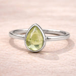 Silver ring with a pear-shaped green natural peridot gemstone on a beige background