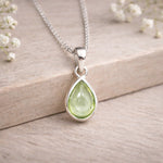 august birthstone teardrop peridot pendant on a silver chain with a wooden background