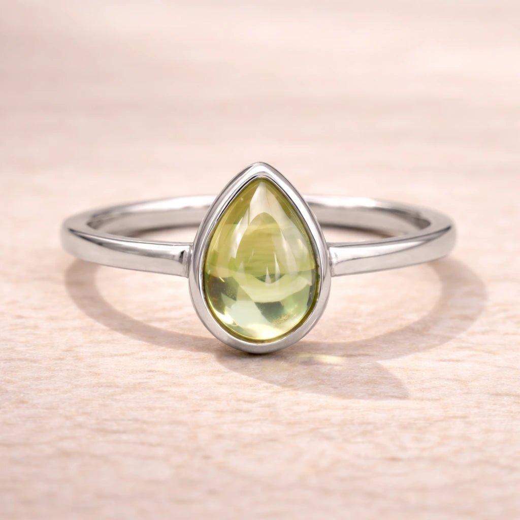 Silver ring with a green teardrop-shaped natural peridot gemstone on a beige background